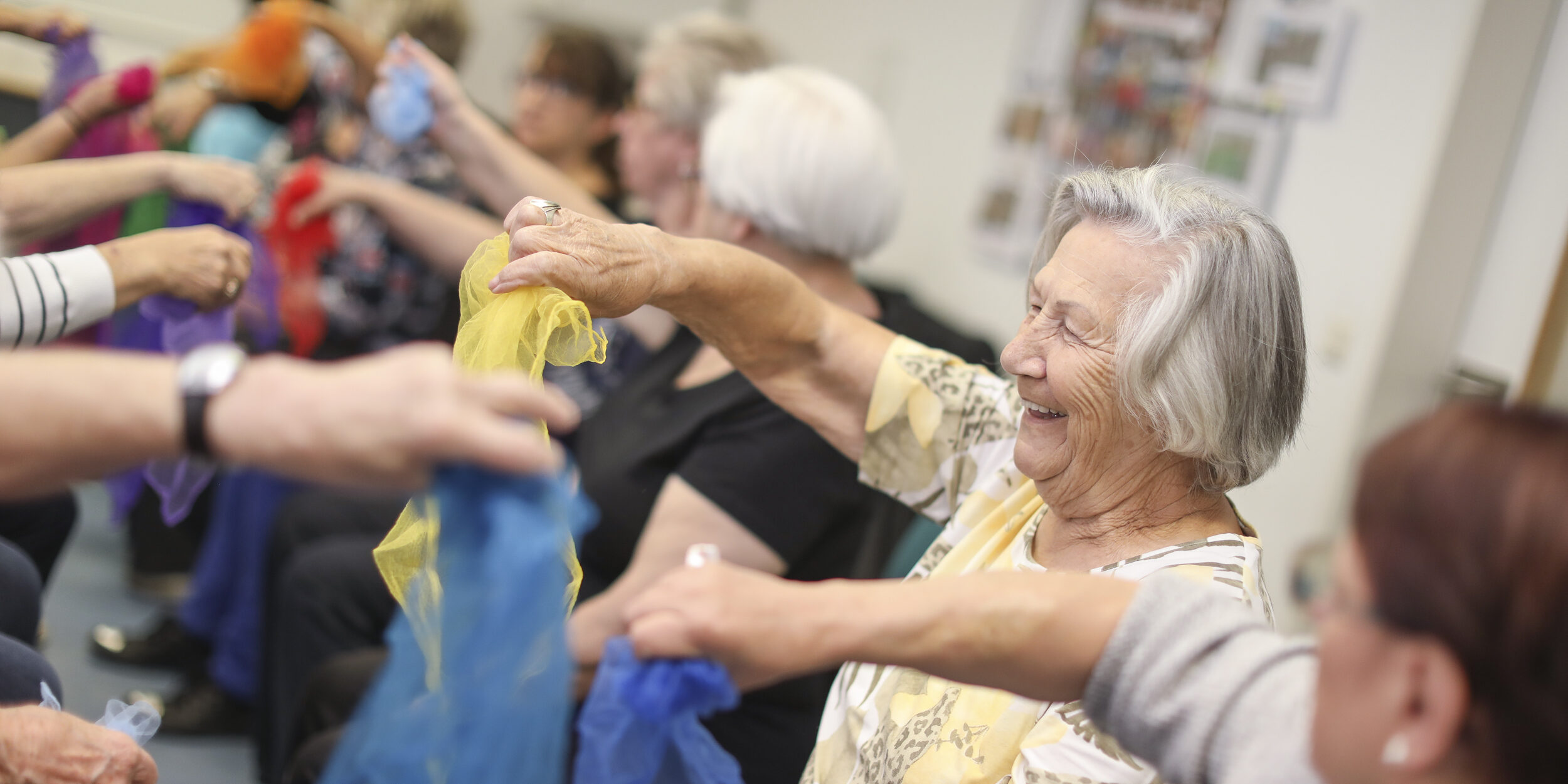 mehrere ältere Personen strecken den Arm aus und halten ein Tuch