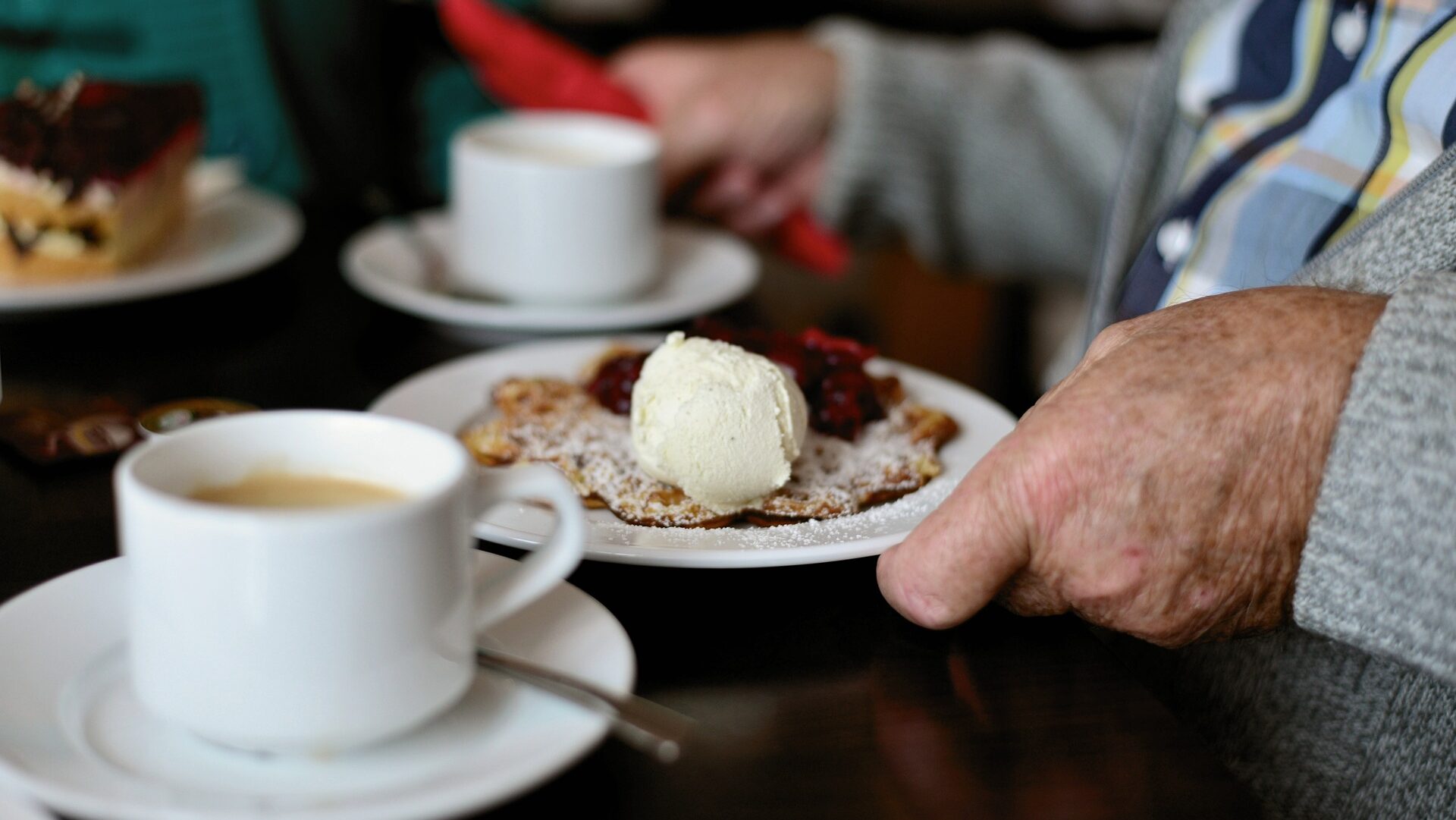 Hand eines Mannes mit Kaffee und Süßspeise