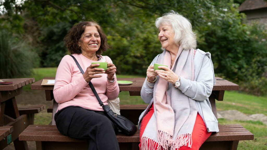 Zwei Frauen unterhalten sich im Freien mit einer Tasse Tee in der Hand.