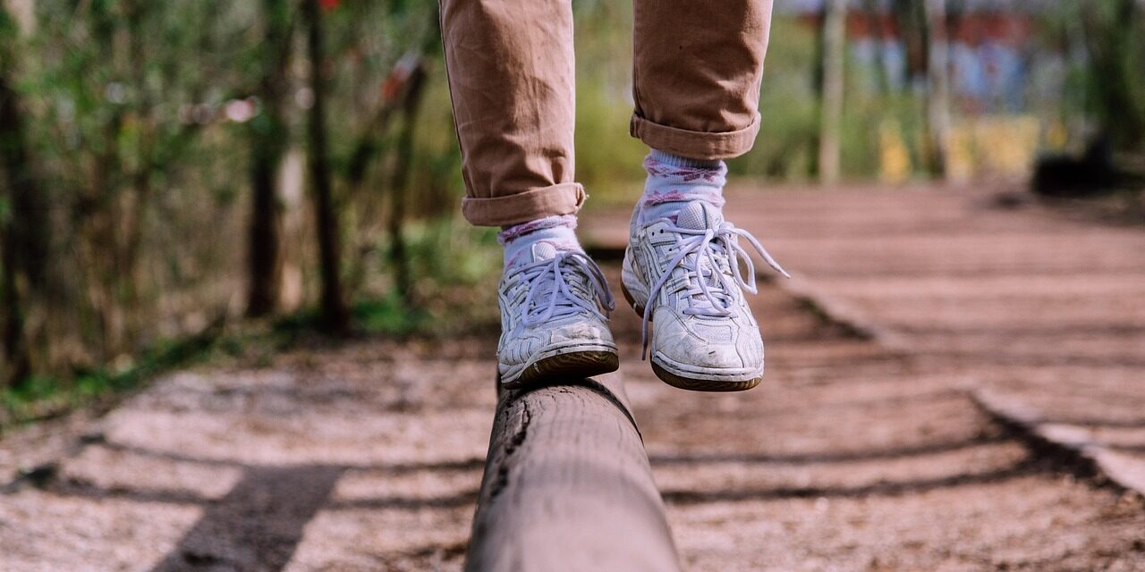 Person balanciert auf einem Baumstamm