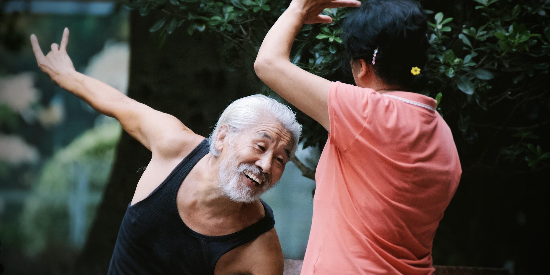 älterer Mann beugt sich hinab, Frau streckt Arm in die Höhe